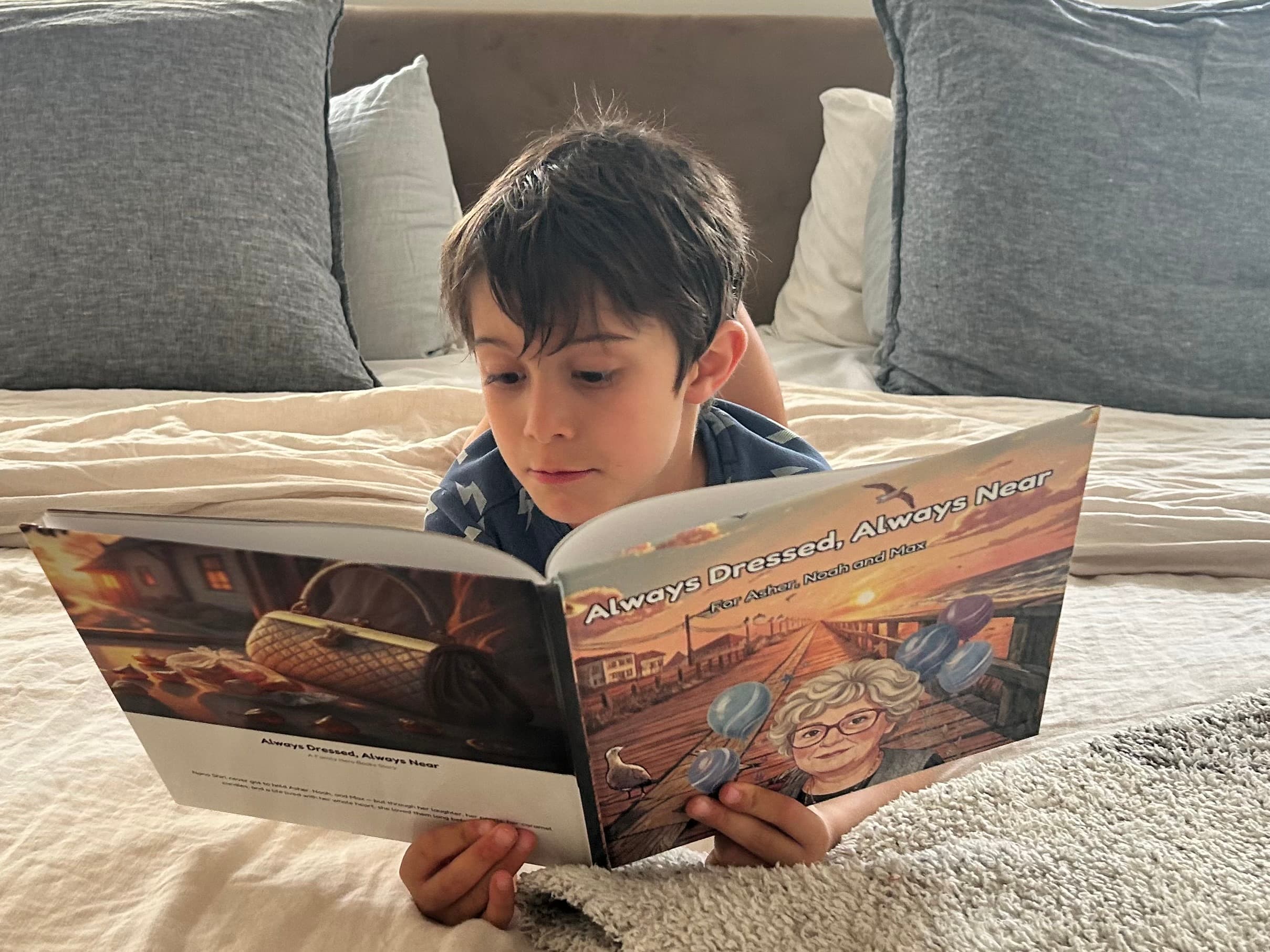 A young boy on a bed reading his Family Hero Book "Always Dressed, Always Near" about his grandmother